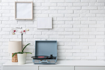 Record player with disk on commode near white brick wall in room