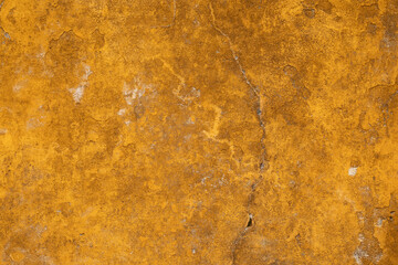 A weathered mustard yellow wall with cracks and peeling paint
