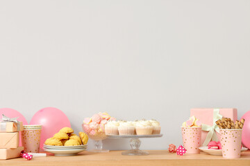 Table with different sweets, gifts and decor for birthday party against white wall