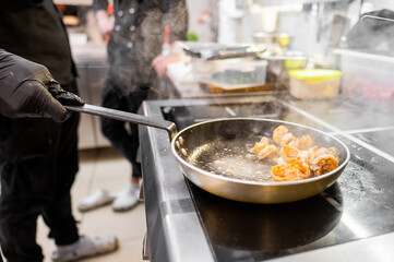 A chef is cooking shrimp in a sizzling pan at a professional kitchen. Steam rises from the pan, creating a dynamic and energetic atmosphere.