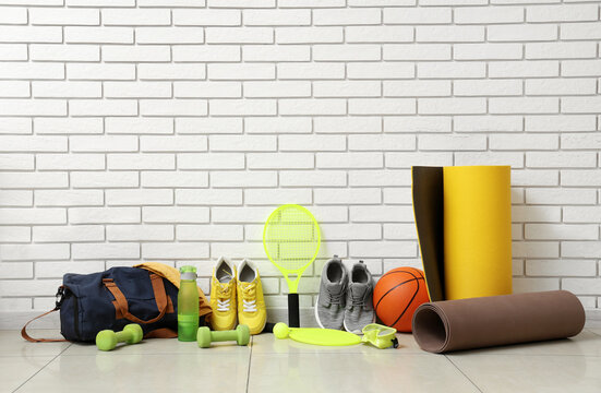 Different sports equipment, bag and sneakers near white brick wall