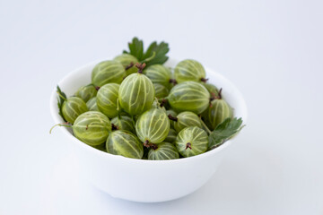 Gooseberry fruit with leaf springs on the white plate over white background. Succulent fresh ripe green organic berries Gooseberry
