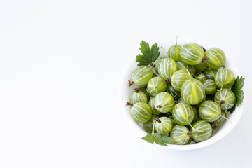 Gooseberry fruit with leaf springs on the white plate over white background. Succulent fresh ripe green organic berries Gooseberry