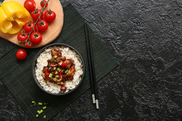 Tasty sweet and sour chicken with rice in bowl, vegetables and chopsticks on black grunge background