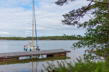 Sailboat moored in the harbor of the island, forest, Finland, Baltic sea, traditional sail yacht in shore marina in Baltic sea, summer vacations in archipelago