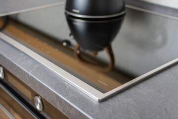 Black kettle reflecting in a glass of an induction stove, closeup image, modern minimalist kitchen...