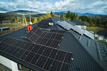 Builders building photovoltaic solar module station on roof of house. Men electricians in helmets installing solar panel system outdoors. Concept of alternative and renewable energy. Aerial view. © anatoliy_gleb