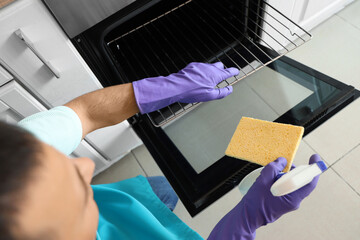 Obraz premium Young man with spray bottle and rag cleaning oven in kitchen, closeup