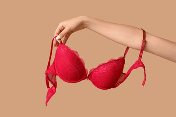 Female hands with stylish lace bra on beige background, closeup