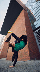 Breakdancer, dressed stylish outfit, performs gravity-defying handstand flip against backdrop of...