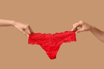Female hand with stylish lace panties on beige background, closeup
