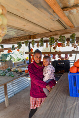 village African woman holding her child , hawker street vendor of fruits, bags of oranges, cabbage,...