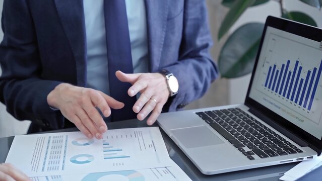 Professional businessman gestures to charts on laptop screen during corporate meeting. Business concept