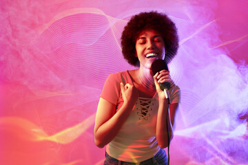 Curly young woman with microphone singing in neon lights on pink background. Audio waveforms near...