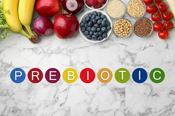 Word Prebiotic and different gut-healthy foods on white marble table, top view