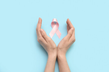 Female hands with pink silk ribbon on blue background. Breast cancer concept