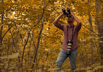 Man using binoculars and camera for bird and animal watching in nature.