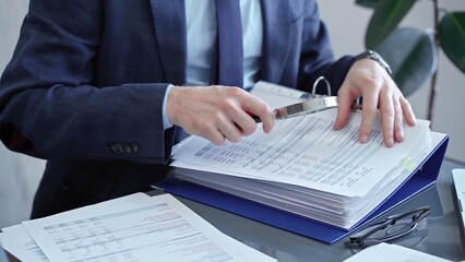 Adult businessman or auditor examining documents with magnifying glass. Professional in a suit...