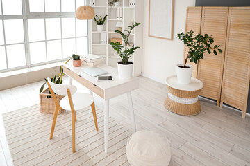 Interior of light office with workplace, shelf unit and folding screen