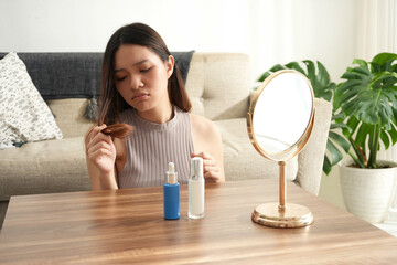 A woman looks at her hair with a concerned expression, possibly worried about its condition. The bright, serene room emphasizes the focus on self-care and hair health.