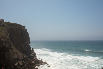 A rugged cliff overlooking a vast blue ocean with crashing waves The scene is serene and awe inspiring