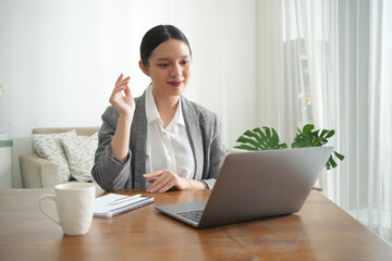 An Asian woman sits at a desk with a laptop and coffee. She is smiling at the camera. Concept of warmth and friendliness