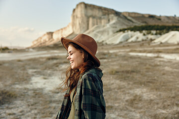 Outdoor adventure woman in plaid shirt and hat standing in front of majestic mountain range