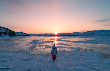 Aerial view on the young woman walking on the blue cracked ice of Baikal at beautiful orange...