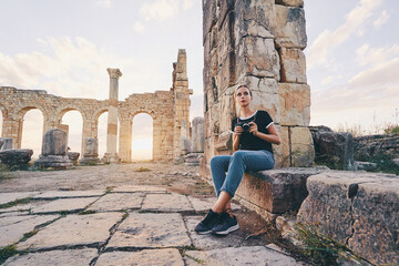 Fototapeta premium Tourism and hobby. Happy young woman taking photo of ancient antique city Volubilis. Traveling by Morocco.