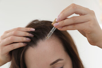 Fototapeta premium Hair loss problem. Woman applying serum onto hairline indoors, closeup