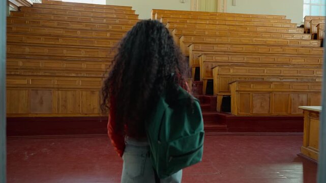 Back view girl student Hispanic female Latina woman lady with backpack walk going come in classroom university college academy big empty auditorium excited wow happy smiling study education lecture