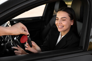 Happy young woman getting key inside her new car