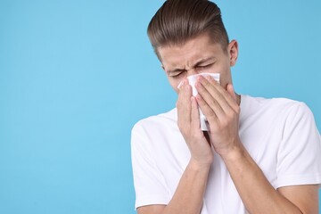 Young man with tissue suffering from sinusitis on light blue background, space for text