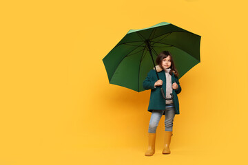 Cute little girl with green umbrella on yellow background. Space for text