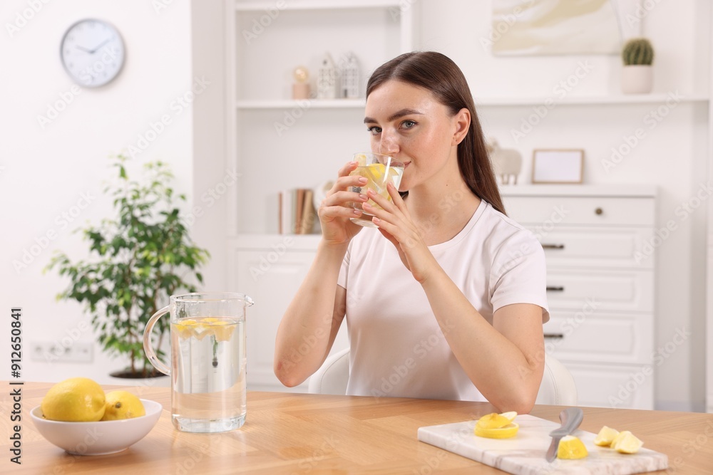 Wall mural Woman drinking water with lemon at table indoors