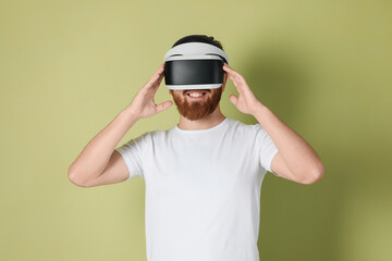 Smiling man using virtual reality headset on pale green background
