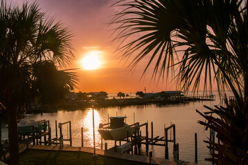 Beautiful sunset over the ocean with boats, buildings, boat docks and palm trees in the scene.