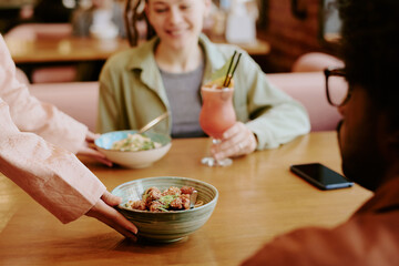 Caucasian woman smiling while eating with friends at cozy cafe table, enjoying different bowls of food and drinks, creating warm and inviting atmosphere