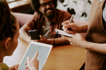 Barista taking order from customers using tablet and notepad at cozy cafe environment smiling and talking off camera enjoying friendly atmosphere