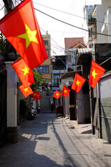 A narrow alleyway in Ho Chi Minh City lined with townhouses, hanging with red Vietnamese flags hung in celebration of national holidays, vibrant and festive atmosphere on Saigon street