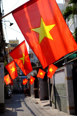 A narrow alleyway in Ho Chi Minh City lined with townhouses, hanging with red Vietnamese flags hung in celebration of national holidays, vibrant and festive atmosphere on Saigon street
