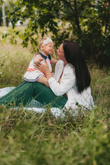 mother and daughter on a summer walk in a green meadow. a woman holds a one-year-old child in her arms