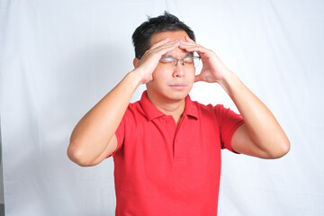 A young Asian man wearing red shirt and glasses is feeling dizzy or stressed. Isolated white...