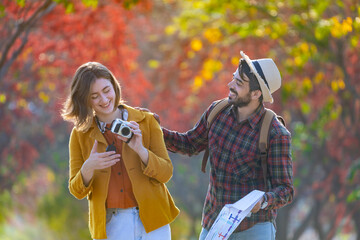 Happy caucasian couple walking together in public park during autumn with maple and beech tree while looking at camera photo for fall color travel destination and family happiness