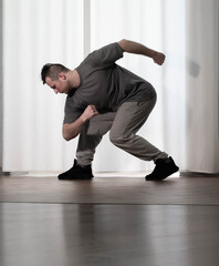 Dance in motion, pose of a man in hip-hop style clothes. Sports dancing guy in training poses. Dance training at home.