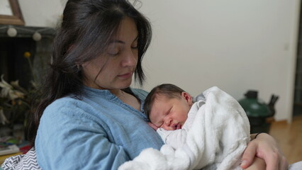 Mother holding her sleeping newborn baby wrapped in a cozy blanket, both peacefully resting, creating a serene and tender moment of bonding and love in a comfortable home setting