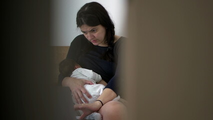 Mother holding newborn baby while working on a laptop, balance between parenthood and professional...