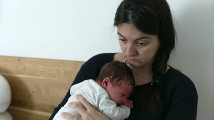 Mother multitasking while working on a laptop, holding a newborn baby in her lap, showcasing the...