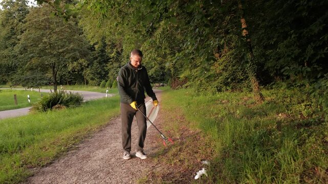 Nice man picking up litter in nature using a trash picker and a garbage bag. Volunteer doing environmental service in his leisure time