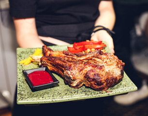 Waiter carrying grilled rib on stone tray with beautiful serving